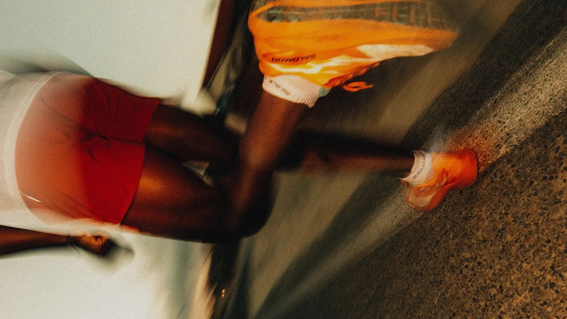 Person jogging on a road wearing bright orange running shoes and red shorts.